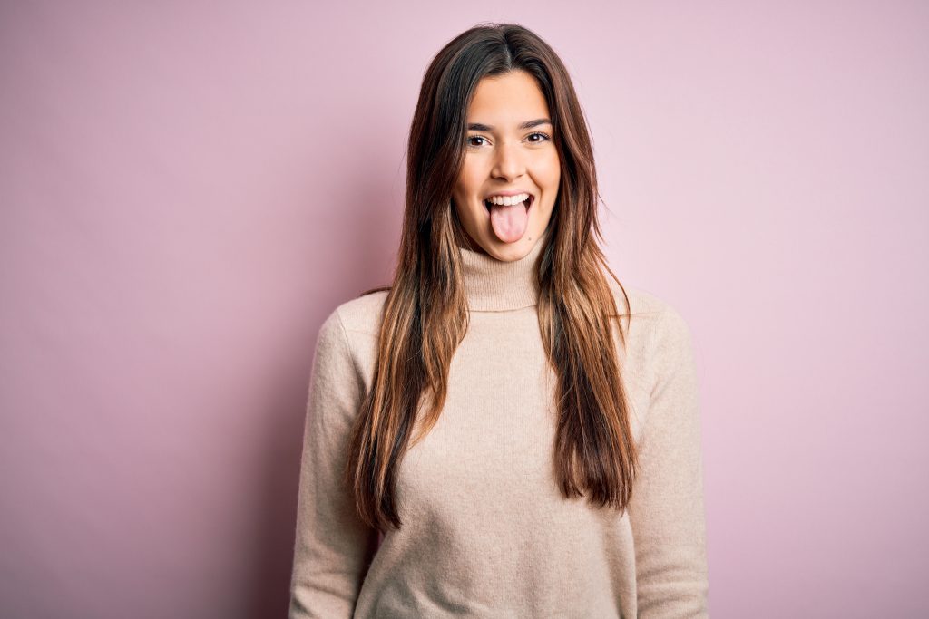 Young beautiful girl wearing casual turtleneck sweater standing over isolated pink background sticking tongue out happy with funny expression. Emotion concept.